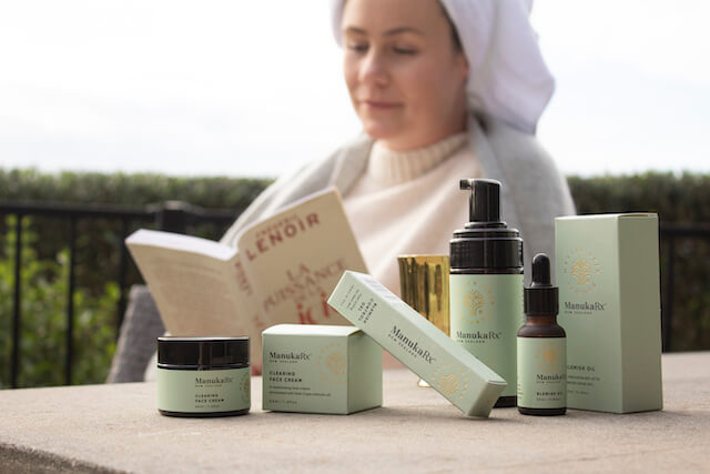Banish Blemishes Naturally with Mānuka Oil image featuring a woman reading outdoors with beautiful clear skin and the ManukaRx Blemish Control product lineup made with Manuka Oil.